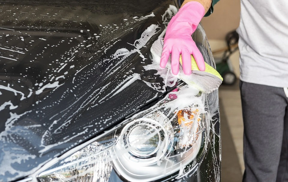 Lavador aplicando espuma y esponja a mano sobre la carrocería de un coche negro a domicilio